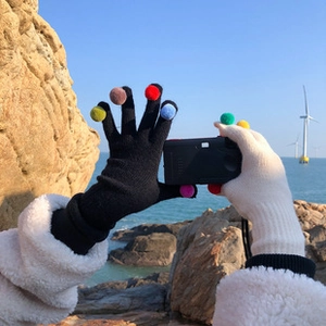 Primer plano de guantes de lana de punto en negro y beige con pompones de colores