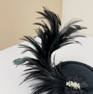 Detail of vintage black pillbox hat with feathers and faux pearl flower accent
