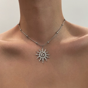 Detail of silver sun pendant necklace on model showing sunburst design and beaded chain