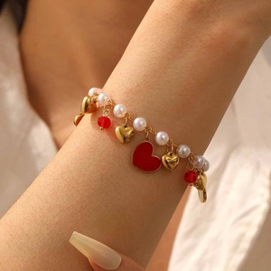 Close-up of heart charm bracelet with pearls and red beads worn on a model wrist