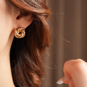 Close-up of golden multi-loop twisted metal knot earring worn by a model in soft lighting
