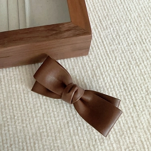 Détail d'une pince à cheveux nœud en cuir PU marron foncé sur tissu blanc texturé