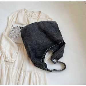 Flat lay of a large dark grey denim tote bag with a white dress and magazine backdrop