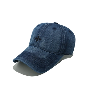 Détail d'une casquette en jean bleu foncé avec une petite broderie de croix noire chic