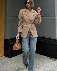 Outdoor shot of a camel-colored fitted blazer paired with blue jeans and a brown bag