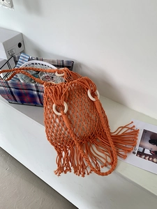 Detail of orange woven tote bag featuring long tassels and natural round wooden handles