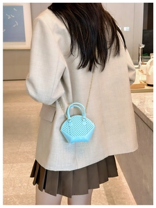 Mini light blue shell bag with woven texture and gold chain worn by a model in a cafe