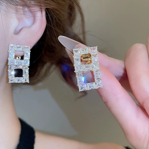 Macro detail of gold-plated square earrings with zircon crystals on a model's ear