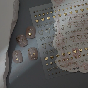 Detail of 3D gold heart and bow nail art stickers with sample manicure display on beige nails