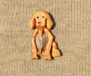 Detail of light brown wooden dog brooch pinned on beige knit sweater fabric