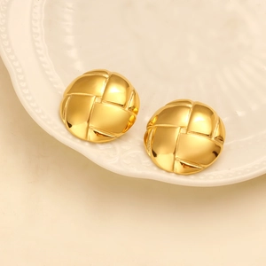 Macro detail of round gold stud earrings with textured grid pattern on white tray