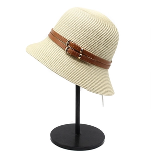 Detail of cream straw bucket hat featuring brown leather straps and gold metal buckles