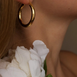Polished 18K gold hoop earrings worn by a model with elegant floral background