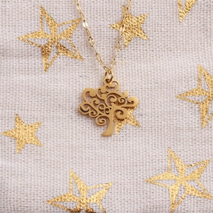 Flat lay of a gold tree of life pendant necklace with hollow design on starry fabric
