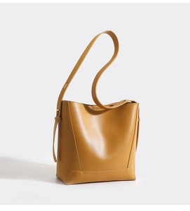 Detailed view of yellow leather bucket bag showing smooth texture and stitching on white backdrop