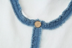 Détail de tricot blanc cousu avec du denim bleu effiloché et un bouton en métal doré