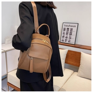 Lifestyle shot of a brown pebbled leather backpack with gold zippers worn by a model