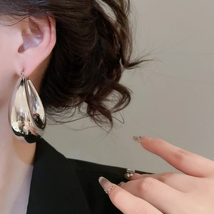 Close-up of a large high-polished silver teardrop earring worn by a female model
