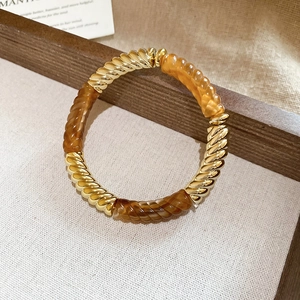 Detailed close-up of golden metal and amber acrylic twisted bangle on textured fabric