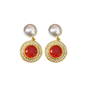 Boucles d'oreilles perles dorées avec zircon rouge et halo de cristaux sur fond blanc