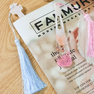 Marque-pages en résine faits main avec fleurs séchées et pompons sur un magazine