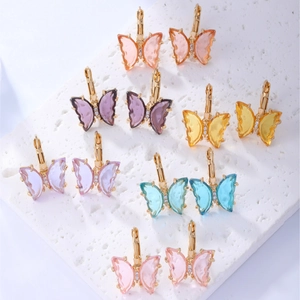 Multiple colorful butterfly stud earrings with resin wings on a white stone base