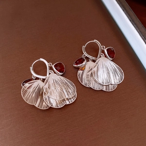 Detail of silver drop earrings with red teardrop stones and fan-shaped metal petals