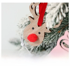 Close-up of wooden reindeer ornament with red pom-pom nose on snowy Christmas tree