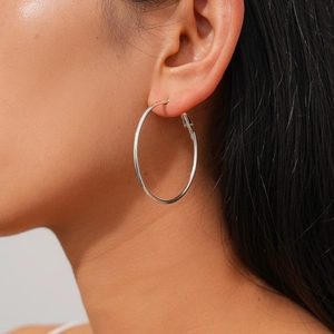 Close-up of a large polished silver hoop earring worn by a model in a minimalist style