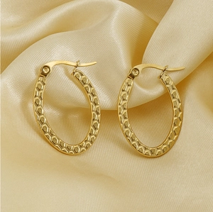 Detail of 18K gold stainless steel oval hoop earrings with textured hammered finish on silk