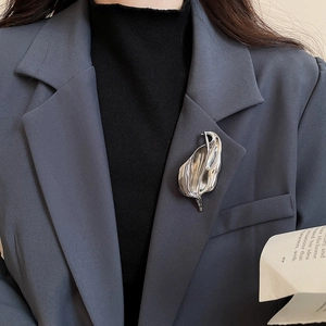Polished silver leaf brooch pinned on a dark grey suit lapel for a modern office look