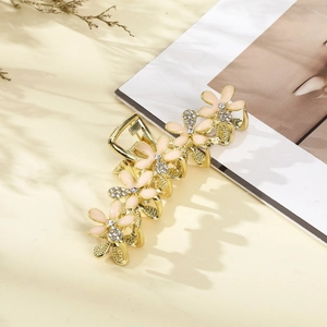 Close-up of golden metal hair claw clip with pink enamel flowers and clear rhinestones