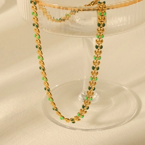 Golden olive leaf necklace with green enamel details displayed on a glass tray