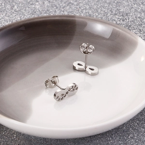 Detailed view of silver infinity symbol and paw print stud earrings on a ceramic dish