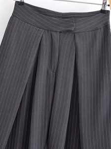 Détail du pantalon gris foncé à fines rayures montrant la taille asymétrique et les plis