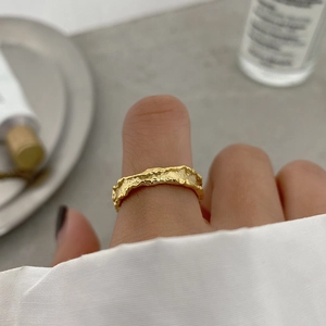 Detail of gold irregular lava texture ring worn on finger with soft lighting