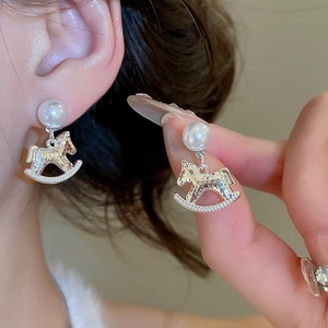 Close-up of pearl stud earrings with rocking horse charms shown on ear and hand