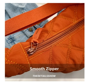 Close-up of orange quilted crossbody bag showing the smooth zipper detail and fabric puller