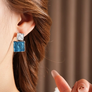 Close-up of double square drop earrings with blue enamel and hammered metallic texture