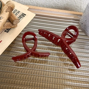 Detail view of two glossy wine red hair claws with metal spring on a glass surface