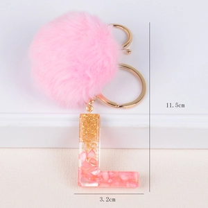 Close-up of pink pom pom keychain with resin letter L featuring gold foil flakes