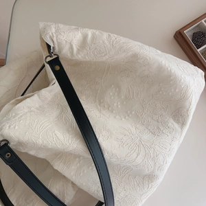 Close-up of beige embroidered tote bag with 3D floral texture and black leather straps
