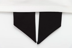 Detail of a black bowtie on a white woven dress with neat stitching and clean textures