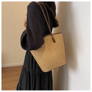 Detail of a large khaki woven straw tote bag with brown leather handles on shoulder