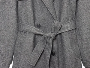 Detail shot of a dark grey wool coat featuring a belted waist and classic black buttons