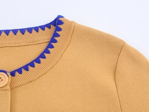 Detail of camel knit cardigan showing blue zigzag trim and round button closure