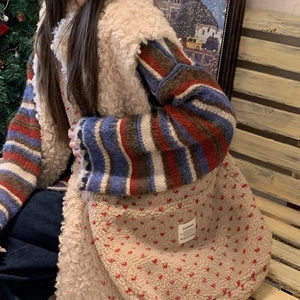 Detail of plush cream crossbody bag with red polka dots and logo patch in winter setting