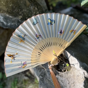 Suzhou silk folding fan with butterfly embroidery and wooden frame on natural rock