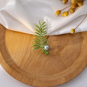 Fashionable green leaf brooch with grey pearl on a wooden tray with silk background