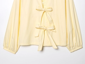 Detailed close-up of pale yellow poplin shirt featuring stylish double bow front tie design